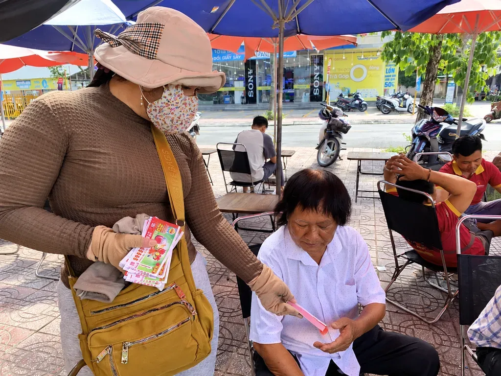 Người bán vé số dạo đưa vé số kiến thiết cho khách hàng tại quán nước ven đường, minh họa hoạt động tiêu thụ vé số miền Nam.
